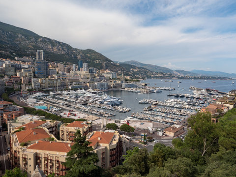 Monaco, july 2019: Monte Carlo cityscape. Real estate architecture on mountain hill background. Many high-rise buildings in downtown area. Yachts moored at town in sunny summer Day