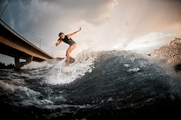 Girl riding on the wakeboard on the river in the background of the bridge rising hands up