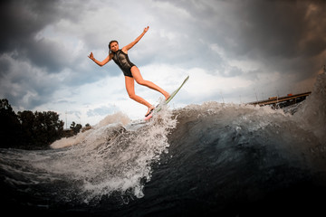Girl jumping on the wakeboard on the river in the background of the bridge rising hands