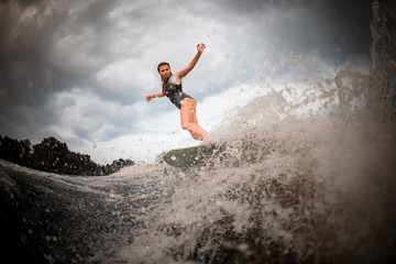 Girl riding on the wakeboard on the river in the background of trees rising hands