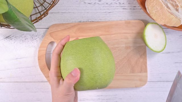 Young asian woman cutting and peeling fresh pomelo to eat kitchen on bright white wooden table and chopping board, top view, overhead view, lifestyle