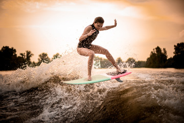 Skinny girl jumping on the wakeboard on the river on the wave in the sunset