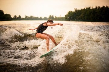 Sporty girl making a trick on the wakeboard on the river in the sunset