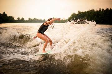 Young girl making a trick on the wakeboard on the river in the sunset