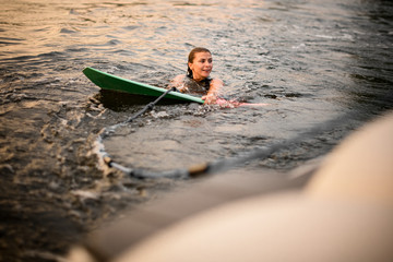Girl swimming holding the wakeboard and a rope of the motorboat