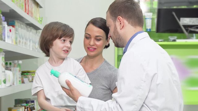 Beautiful woman and her little son talking to pharmacist at drugstore. Attractive woman shopping for medicament with her little son. Pharmacist helping his customers