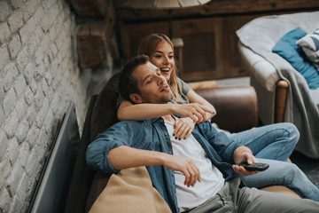 Smiling young couple relaxing and watching TV at home