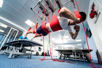 Physiotherapy. Suspension training therapy. Young man doing fitness traction therapy with...