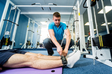 Fototapeta na wymiar Rehabilitation therapy. Young man doing exercises on mat under supervision of physiotherapist.