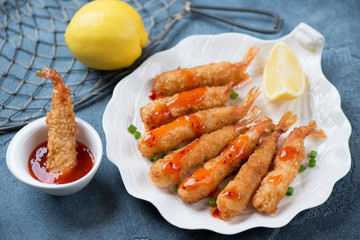 Deep-fried shrimps with breadcrumbs on a shell-shaped plate, studio shot on a blue stone surface