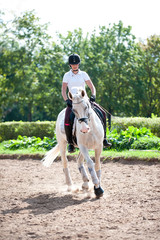 Young pretty teenage girl equestrian practicing horseback riding on manege