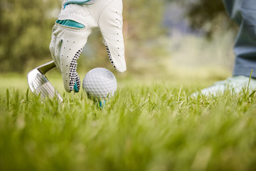 Hand in glove placing golf ball on tee