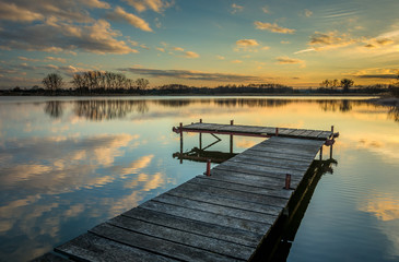 Pier on the lake, reflection of clouds in the water after sunset