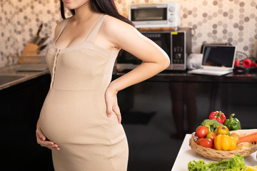 Pregnant woman in dress holds hands on belly on a white background. Pregnancy, maternity, preparation and expectation concept. Close-up, copy space, indoors. Beautiful tender mood photo of pregnancy