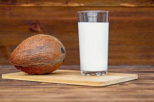 Coconut milk. A glass of skim milk next to coconut close-up on a wooden table.