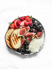 Snack appetizers tapas plate with cheese, figs, olives, berries on a light background, top view