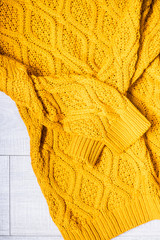 Yellow knitted sweater on a wooden light background, top view. Flat lay, copy space