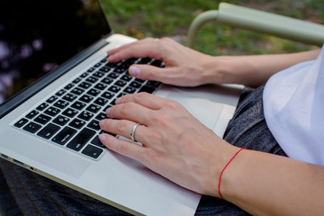 A woman is typing on a laptop keyboard. Online business outdoors. Girl freelancer works in the park. Workspace. Modern business day. Remote work. Lifestyle. Mobile device. Laptop buttons closeup