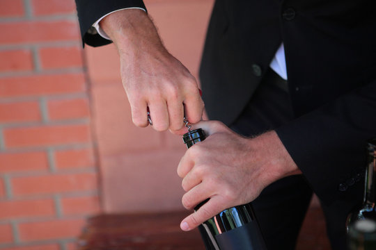Sommelier holds a bottle of wine and opens it with a corkscrew. Photo without a face. Hands close up. Wine tasting concept.