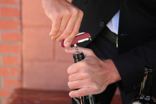 Corkscrew in the hands of a sommelier who opens a bottle of wine. Photo without a face. Hands close up. Wine tasting concept.