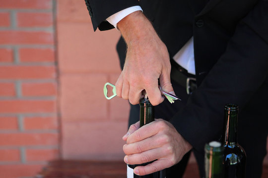 Sommelier holds a bottle of wine in his hand and opens it with a corkscrew. Photo without a face. Hands close up. Wine tasting concept.