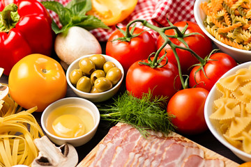 Italian food ingredients - pasta, vegetables, mushrooms, bacon, eggs, olives. Flat lay on dark wooden background