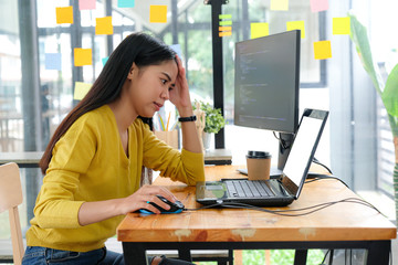 Asian female programmer wears a yellow shirt, looks at the laptop screen and shows a serious pose.