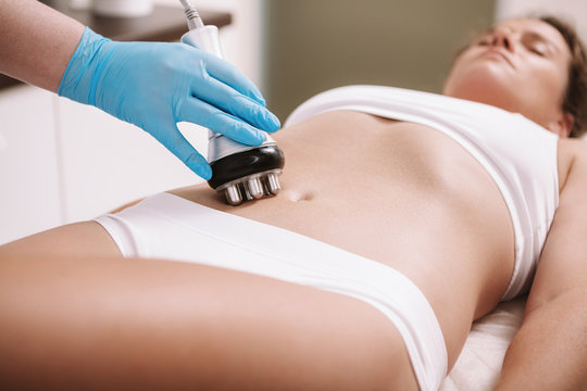 Woman enjoying rf-lifting procedure on her stomach skin at beauty clinic. Professional beautician using rf-lifting machine, tightening skin on the belly of a female client