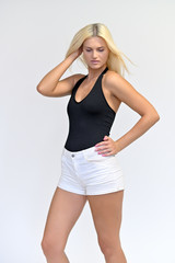 Vertical portrait of a cute girl, a young blonde woman with beautiful curly hair in a black T-shirt and white shorts on a white background. Beauty, brightness, smile, emotions.