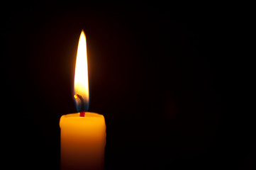 Close-up of single burning candle on black background. Copy space. Horizontal shot.