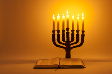 Open Holy Bible and Menorah with candlelight. Isolated on golden background. Copy space. Horizontal shot.