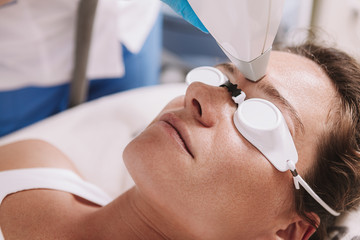 Close up of a woman wearing protective goggles, getting facial hair removed by beautician