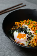 Drunken spicy noodles in black bowl with Onsen egg on the concrete table.