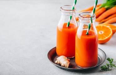 Fresh carrot, ginger and orange drink in glass bottles on a gray stone background