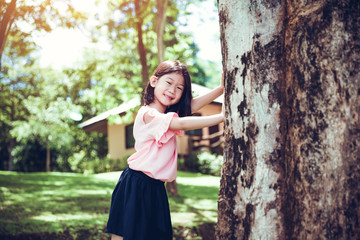 Cute little asian girl under big tree outdoor in the park.