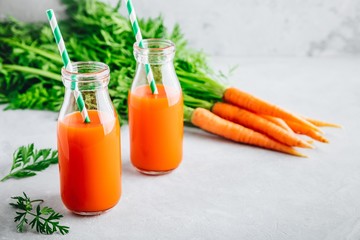 Fresh detox carrot juice in glass bottles on a gray stone background