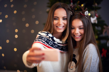 Obraz na płótnie Canvas Mother and daughter celebrating Christmas at home and taking selfie