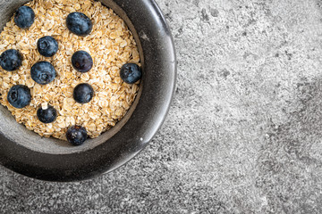 top view of rolled oats, oatmeal and blueberries in stone bowl on kitchen counter