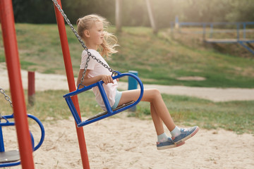 Fototapeta na wymiar Image of child on swing in playground outdoors, liitle girl with ponytail and casual clothing, looking away with concentarted facial expression, waiting friend or mother, swinging. Childhood concept.