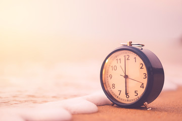 Clock on sand beach with smooth wave background.