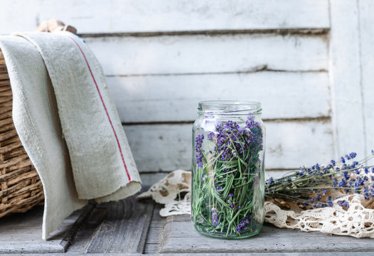 A glass jar full of freshly harvested lavender blossoms in vintage traditional environment with homemade corf and towel
