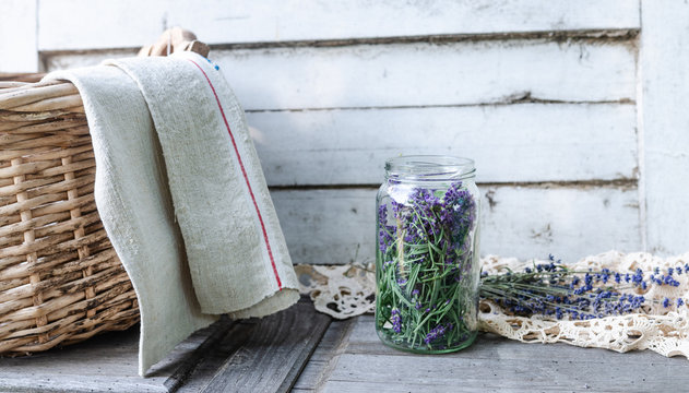 A glass jar full of freshly harvested lavender blossoms in vintage traditional environment with homemade corf and towel