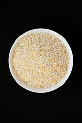 Organic Arborio rice in a white bowl on a black background, top view. Flat lay, overhead, from above.
