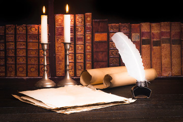 Inkwell with pen, scroll of parchment, and candle against the background of bookshelves with old books