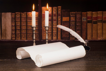 Inkwell with a pen on a countertop made of old boards, scroll and candle, against the background of shelves with old books