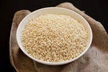 Organic Arborio rice in a white bowl on a black background, low angle view. Close-up.