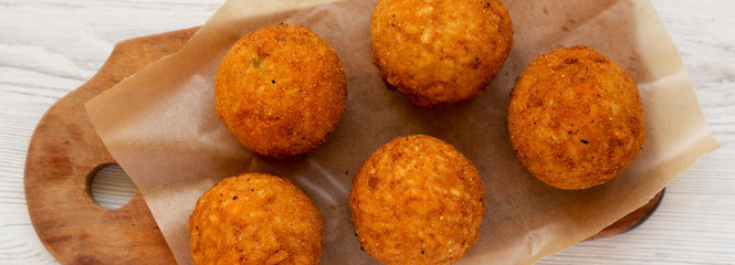 Homemade fried Arancini on a rustic wooden board on a white wooden surface, top view. Italian rice balls. Close-up.