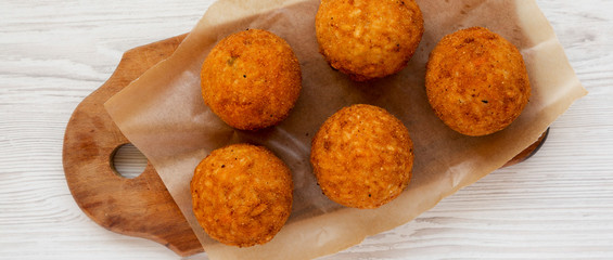 Top view, homemade fried Arancini on a rustic wooden board on a white wooden background. Italian rice balls. Close-up.