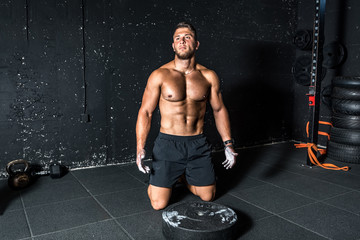 Fototapeta na wymiar Young strong muscular man with big muscles sitting on the gym floor after heavy workout training with barbell weight plate