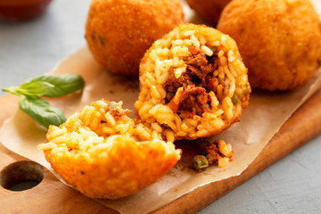 Homemade fried Arancini with basil on a rustic wooden board, side view. Italian rice balls....